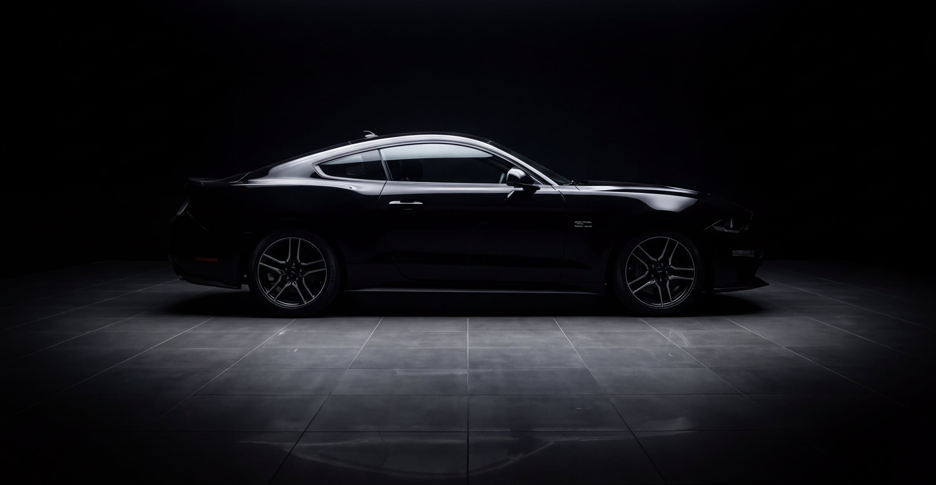 A black Mustang GT in a dark studio, its lines picked out by a single overhead light